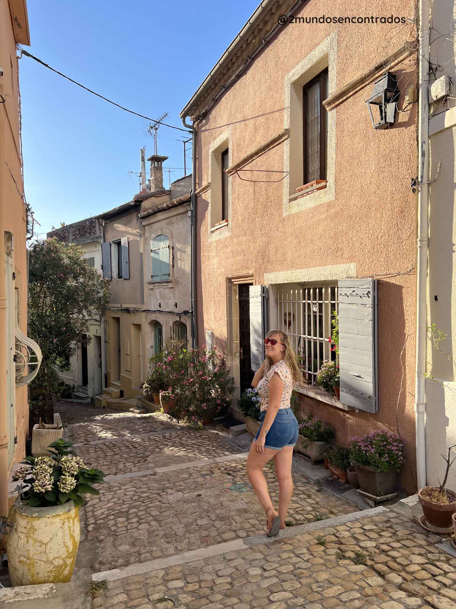 Eva caminando por una calle empedrada con fachadas de colores pastel en el casco histórico de Arles, Provenza.