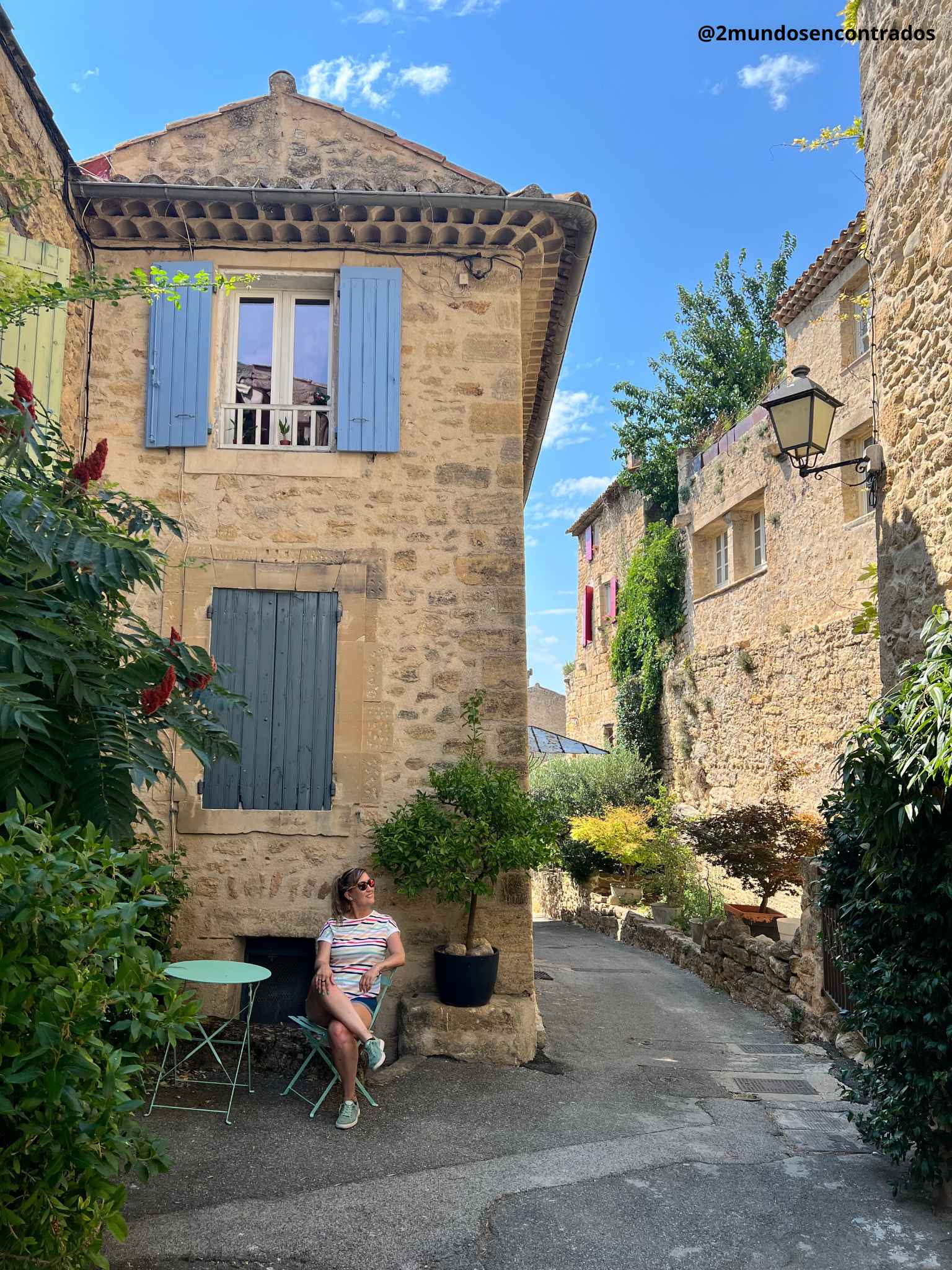 Eva sentada en una terraza junto a una casa de piedra con contraventanas azules en Ansouis, Provenza. Qué ver en la Provenza en 11 días