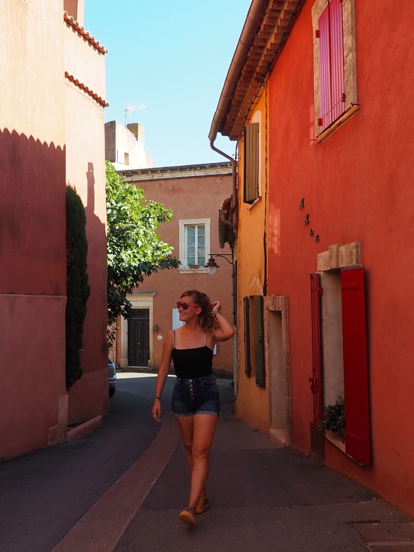 Eva paseando por una callejuela con fachadas de tonos ocres, rojos y amarillos en el pintoresco pueblo de Roussillon, en el sur de Francia.