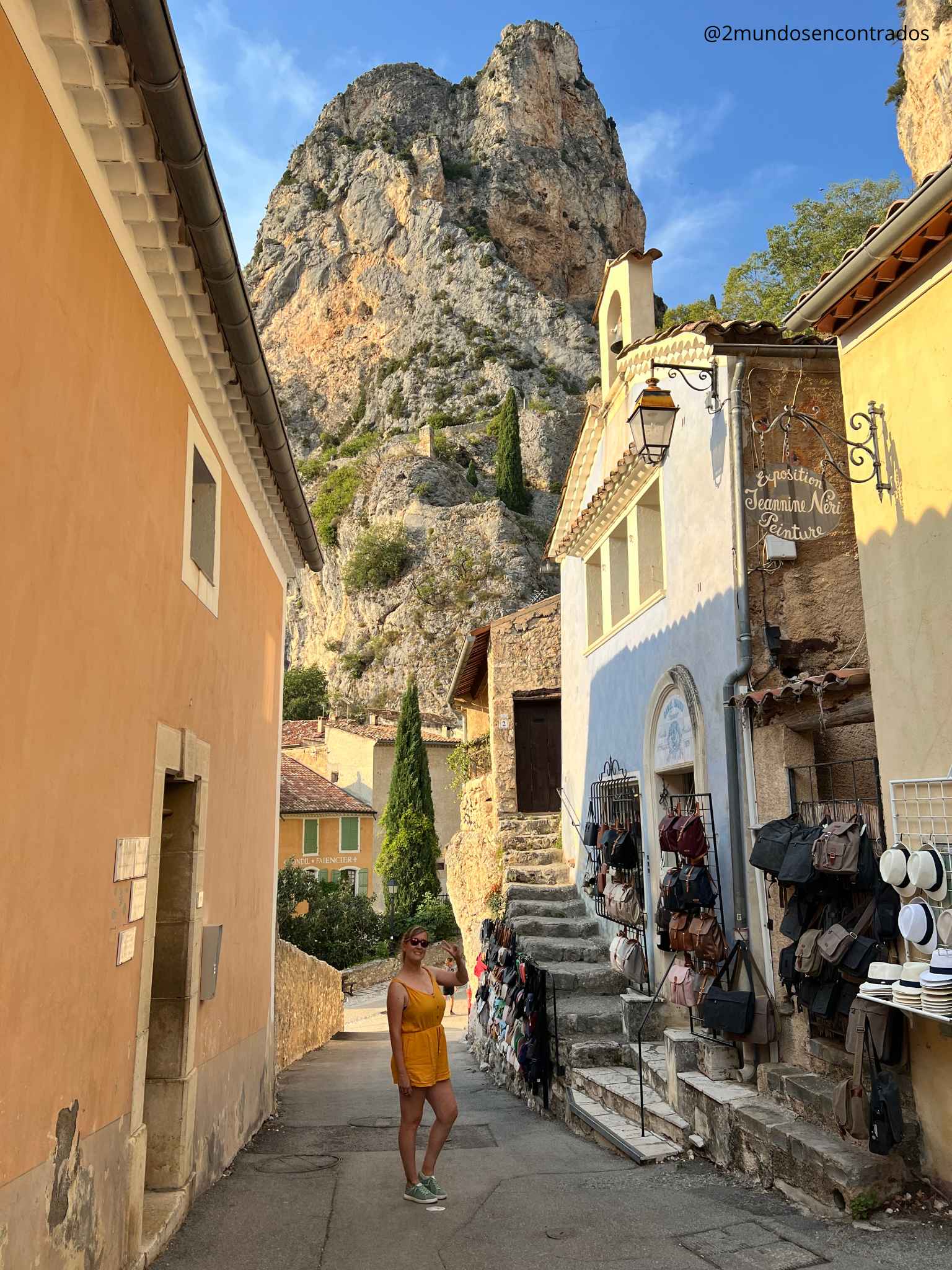 Eva posando en una calle de Moustiers-Sainte-Marie con las impresionantes montañas de roca caliza y las casas provenzales como telón de fondo. Qué ver en la Provenza en 11 días