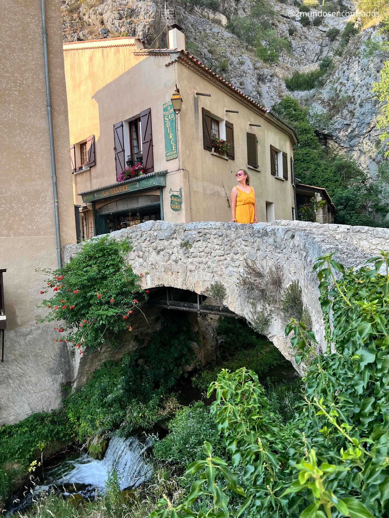 Puente de piedra sobre un arroyo con cascada en Moustiers-Sainte-Marie, uno de los pueblos más bonitos de la Provenza, rodeado de casas tradicionales y naturaleza.