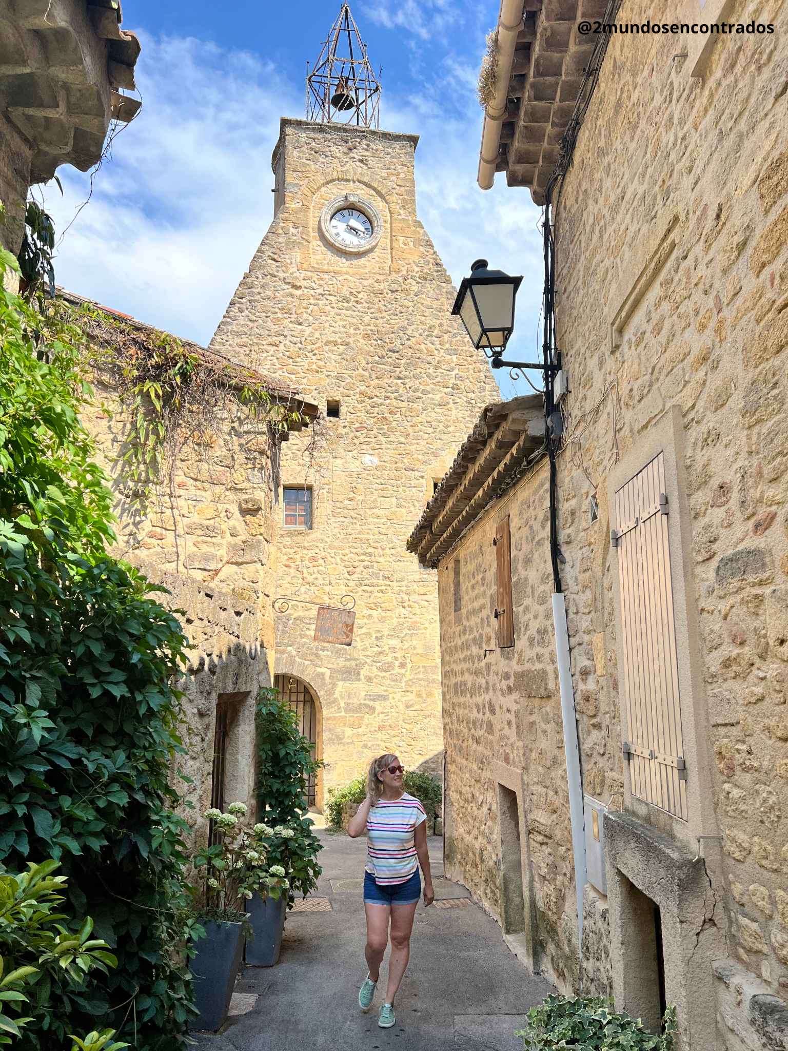 Eva caminando por una calle empedrada frente a la antigua torre del reloj en Ansouis, Francia. Qué ver en la Provenza en 11 días