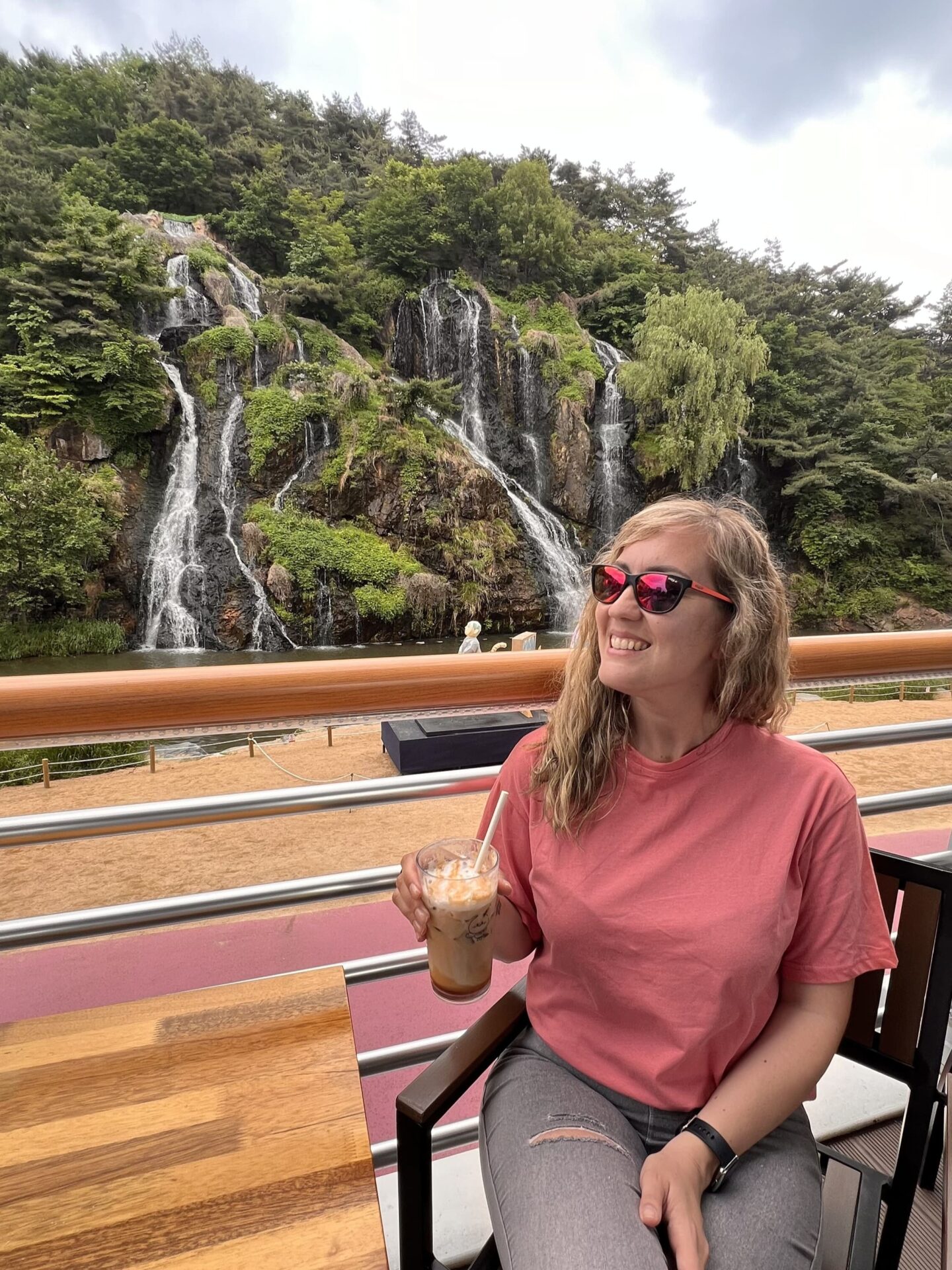 Viajera tomando un café helado en la terraza del Café Pokpo, con la cascada Pokpo de Seúl de fondo, uno de los rincones más sorprendentes de la ciudad.