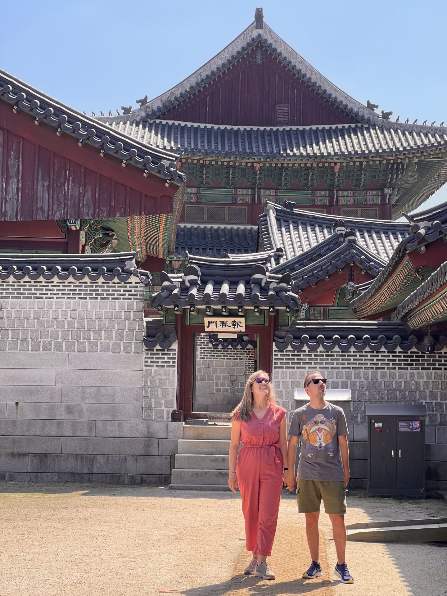 Dos visitantes caminando frente a la arquitectura tradicional del Palacio Gyeongbokgung en Seúl bajo un cielo despejado.