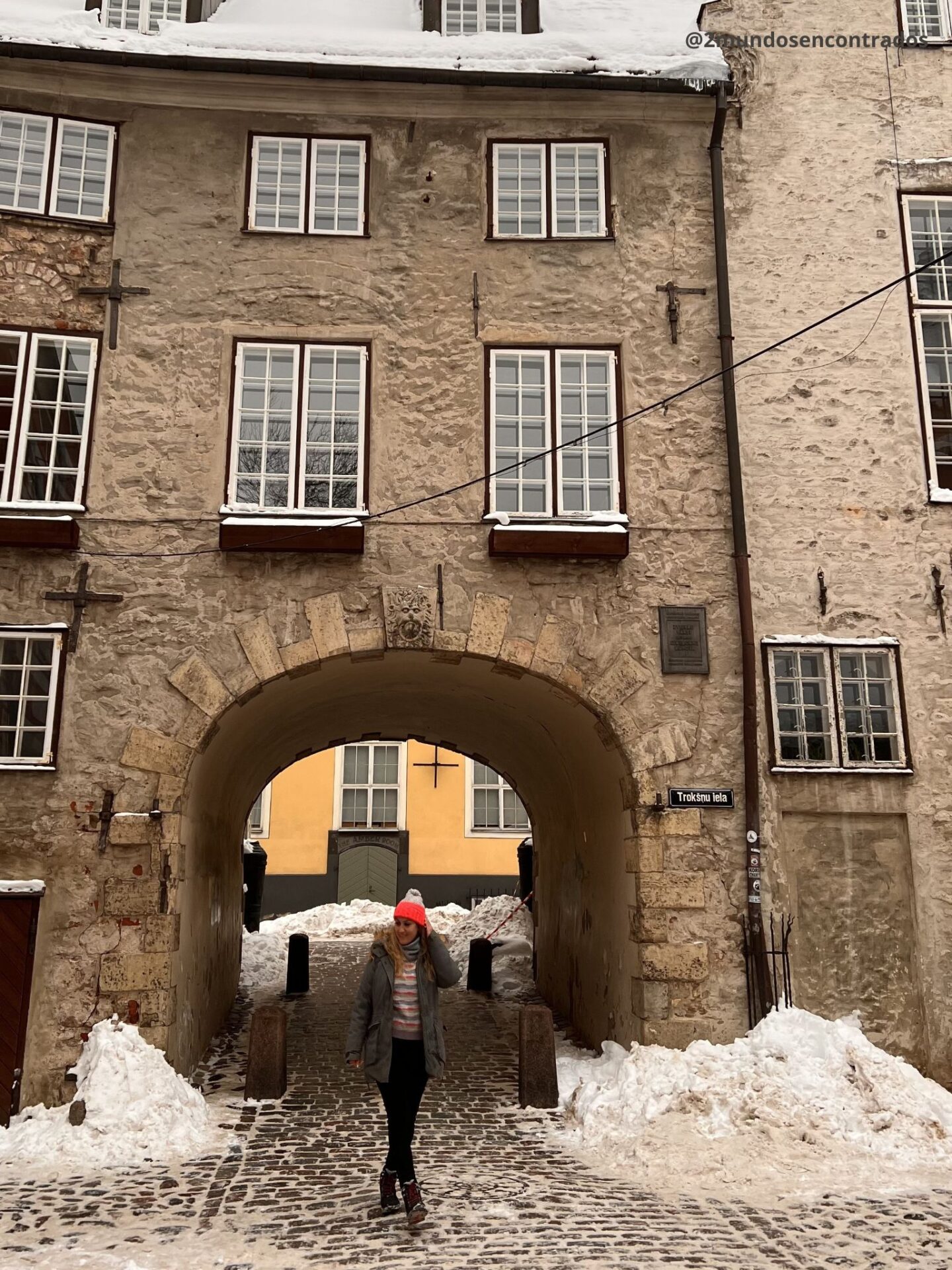 Viajera caminando bajo un arco medieval cubierto de nieve en la Ciudad Vieja de Tallin durante el invierno.