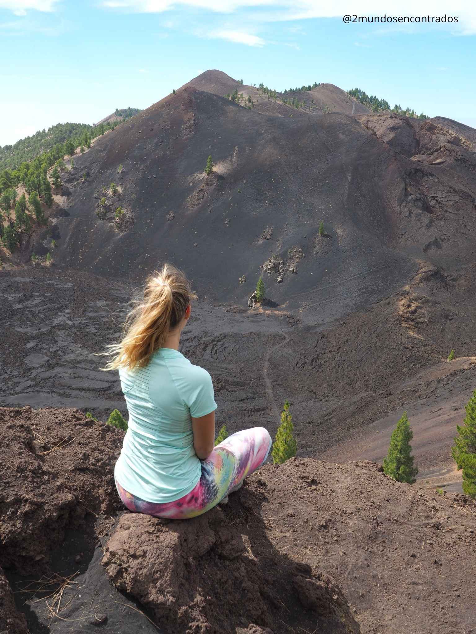Eva sentada en el borde observando el paisaje de piroclastos y pinos canarios en un cráter volcánico de La Palma.