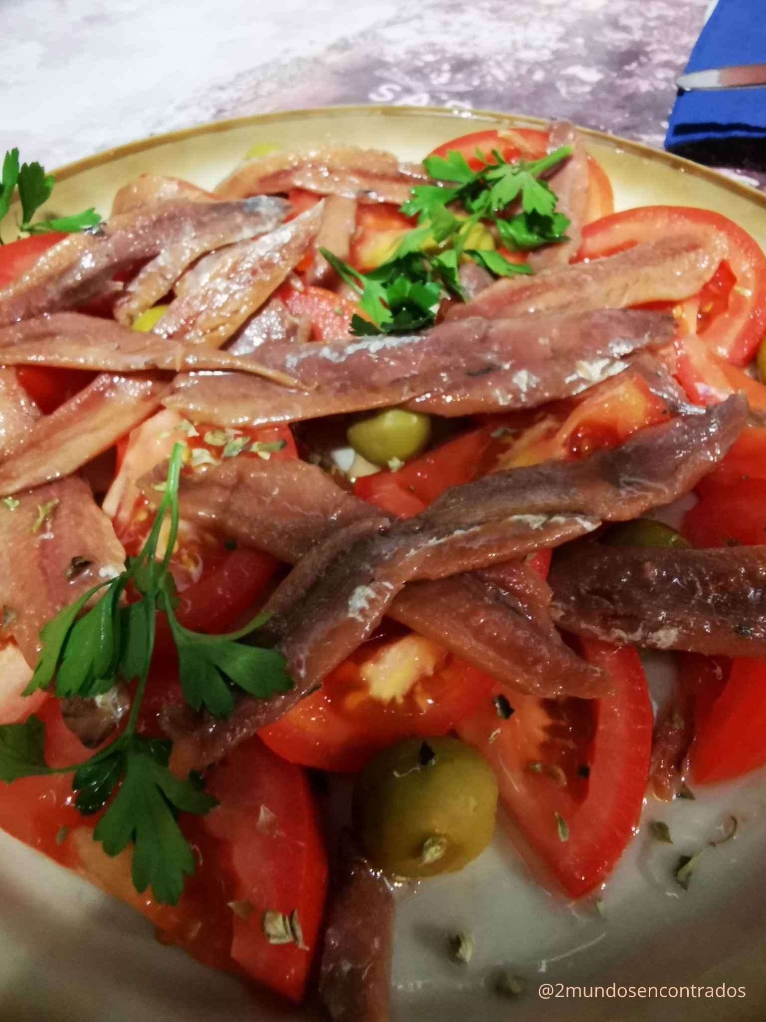 Plato de ensalada de tomate fleteado con anchoas del Cantábrico, aceitunas verdes y perejil fresco.