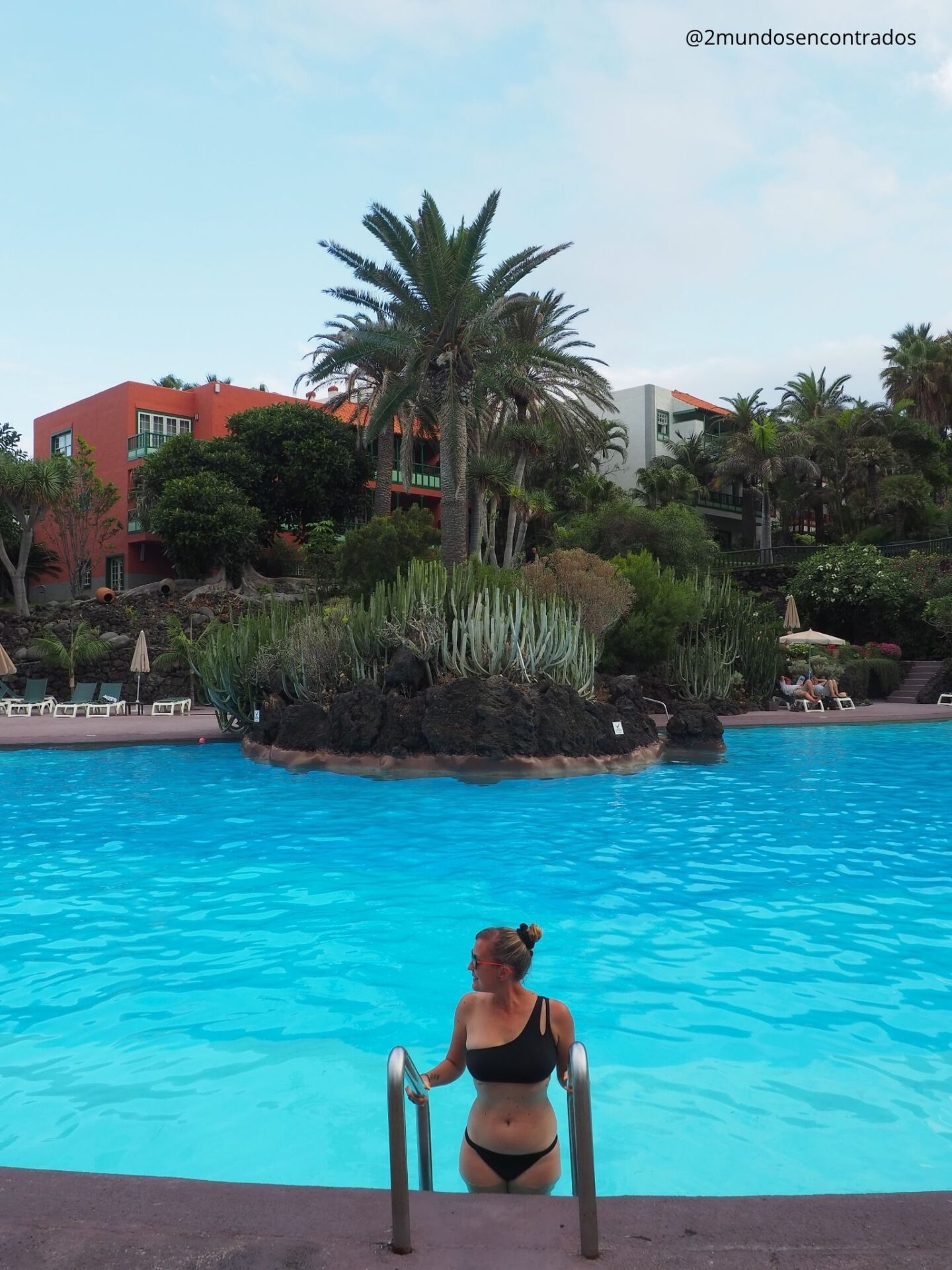 Eva saliendo de una piscina de agua azul rodeada de palmeras y vegetación tropical en un hotel de La Palma.