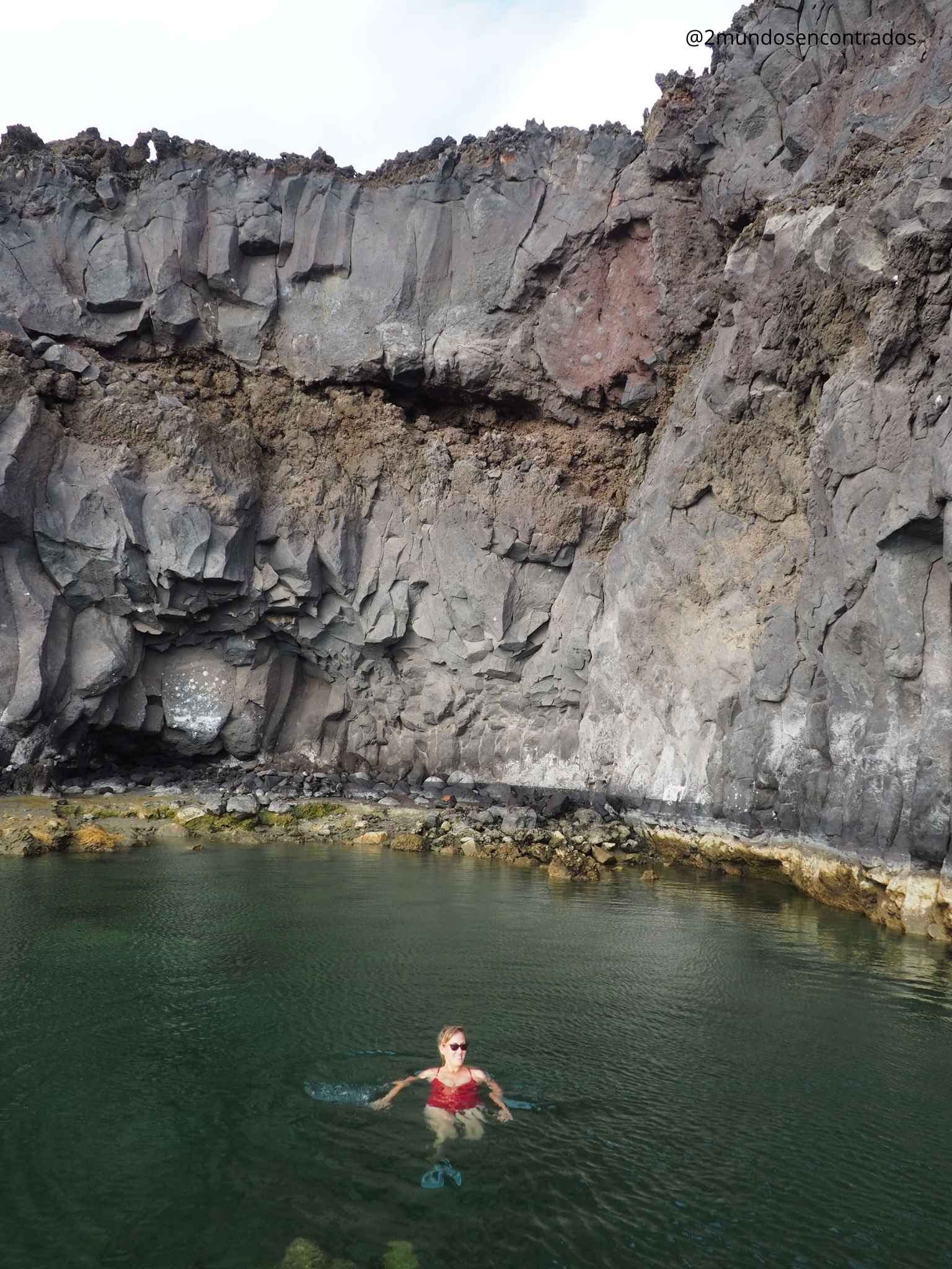 Mujer nadando en una piscina natural protegida por una enorme pared de roca volcánica en La Palma.