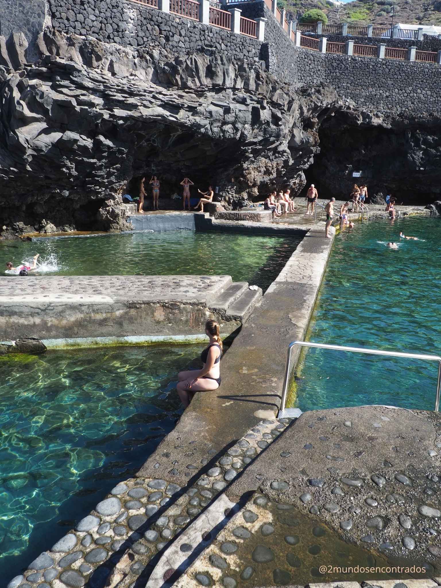 Eva sentada al borde de una piscina natural de agua cristalina rodeada de rocas volcánicas en La Palma.