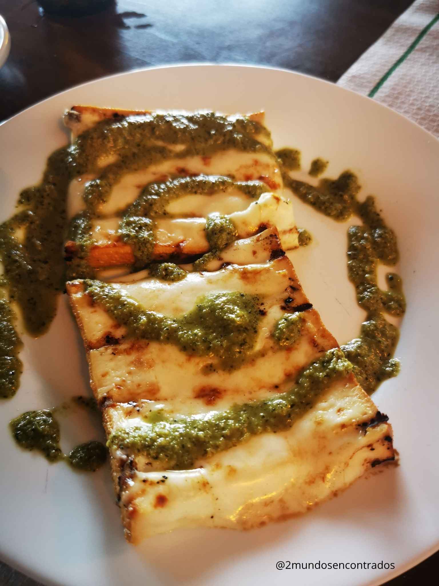 Queso a la plancha bañado con salsa pesto verde sobre plato blanco