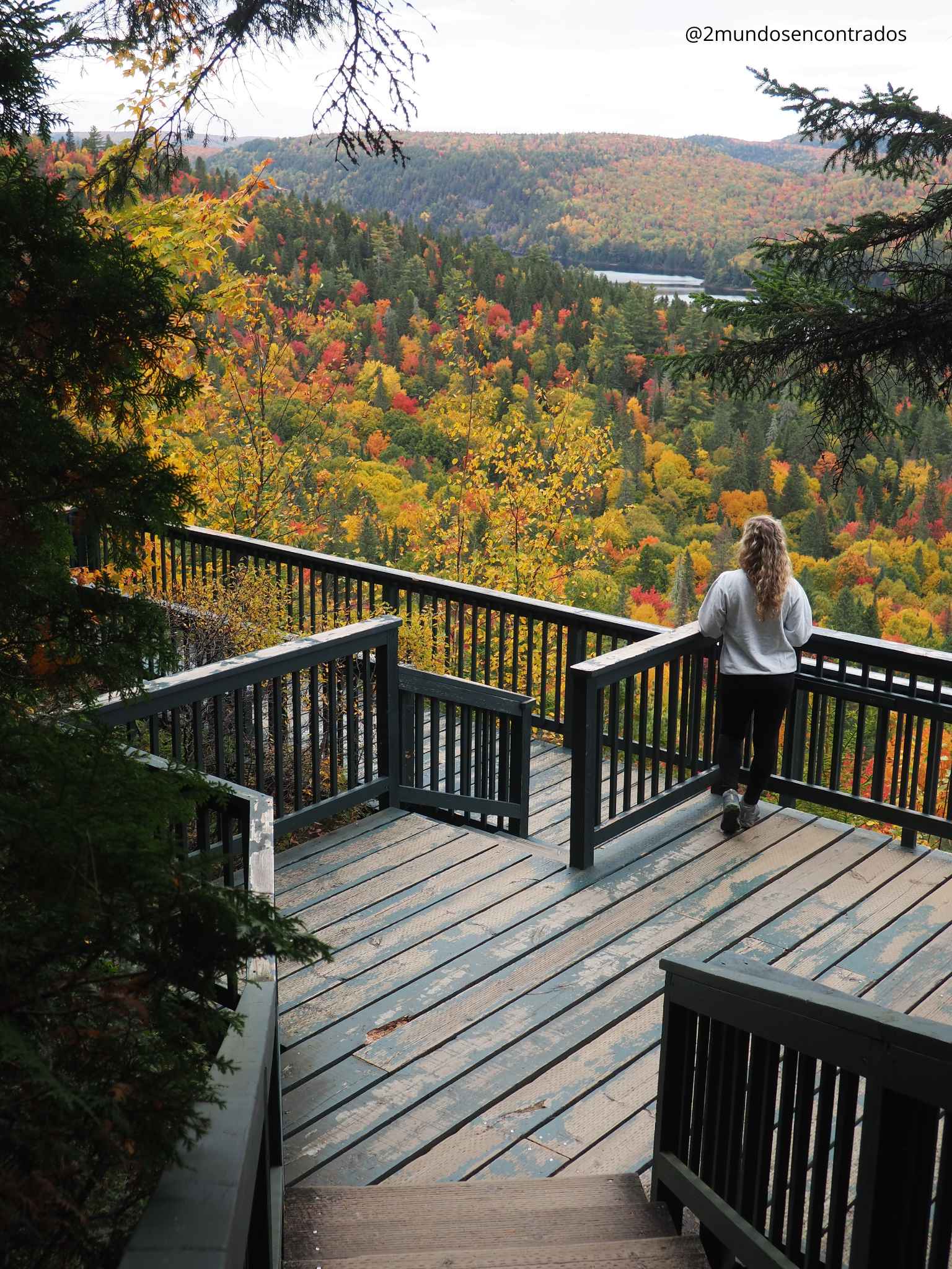 Eva en la plataforma de madera del Belvédère Le Passage contemplando las vistas del lago y bosque de otoño.